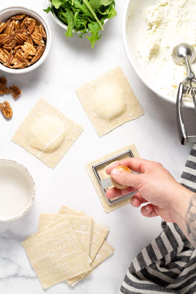 Overhead shot of a white marble counter top with wonton ravioli being stamped with a ravioli stamp