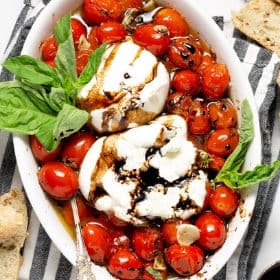 Overhead shot of a white platter filled with roasted tomatoes and burrata garnished with basil