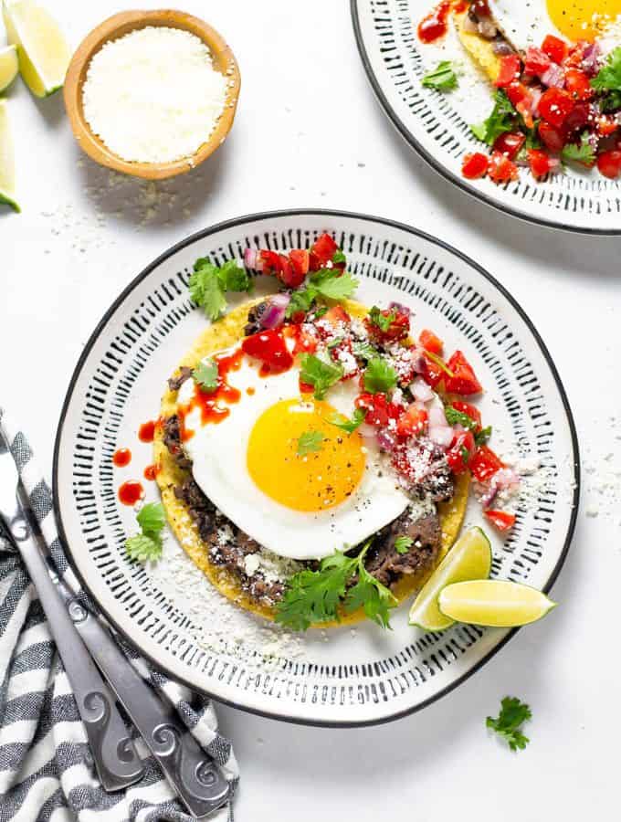 Mexican breakfast tostada on a white and black plate garnished with fresh cilantro and pico de gallo