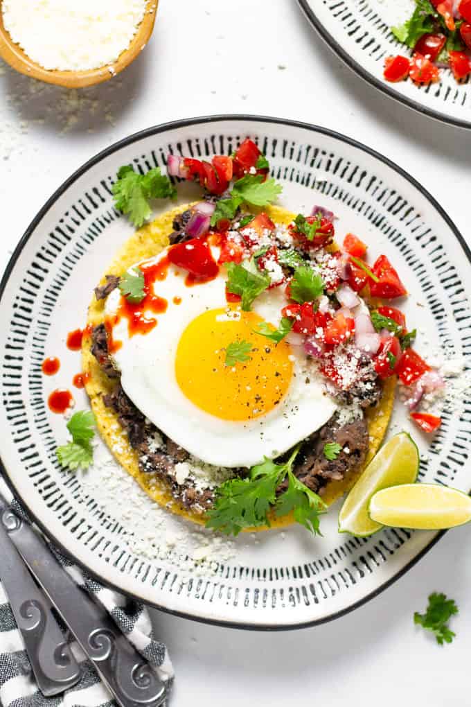 Mexican breakfast tostada on a white and black plate garnished with fresh cilantro and pico de gallo