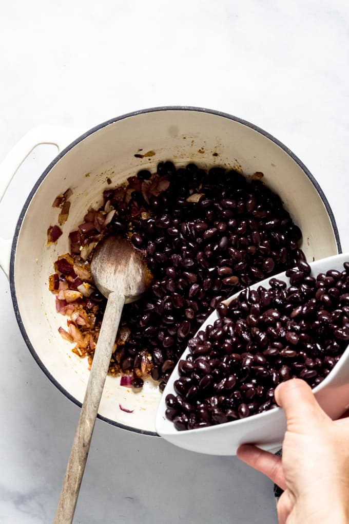 Overhead shot of a white pot with black beans being poured into it