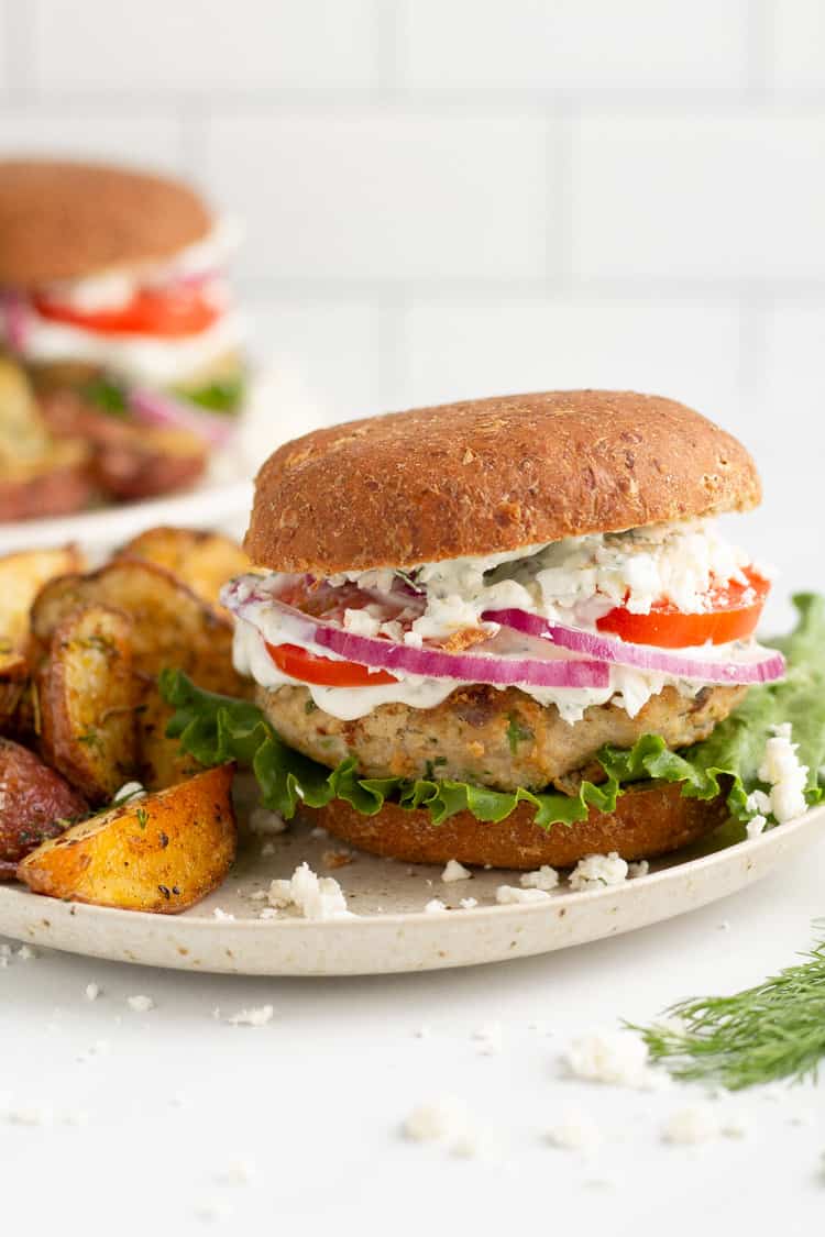 White plate with a Greek turkey burger and potato wedges