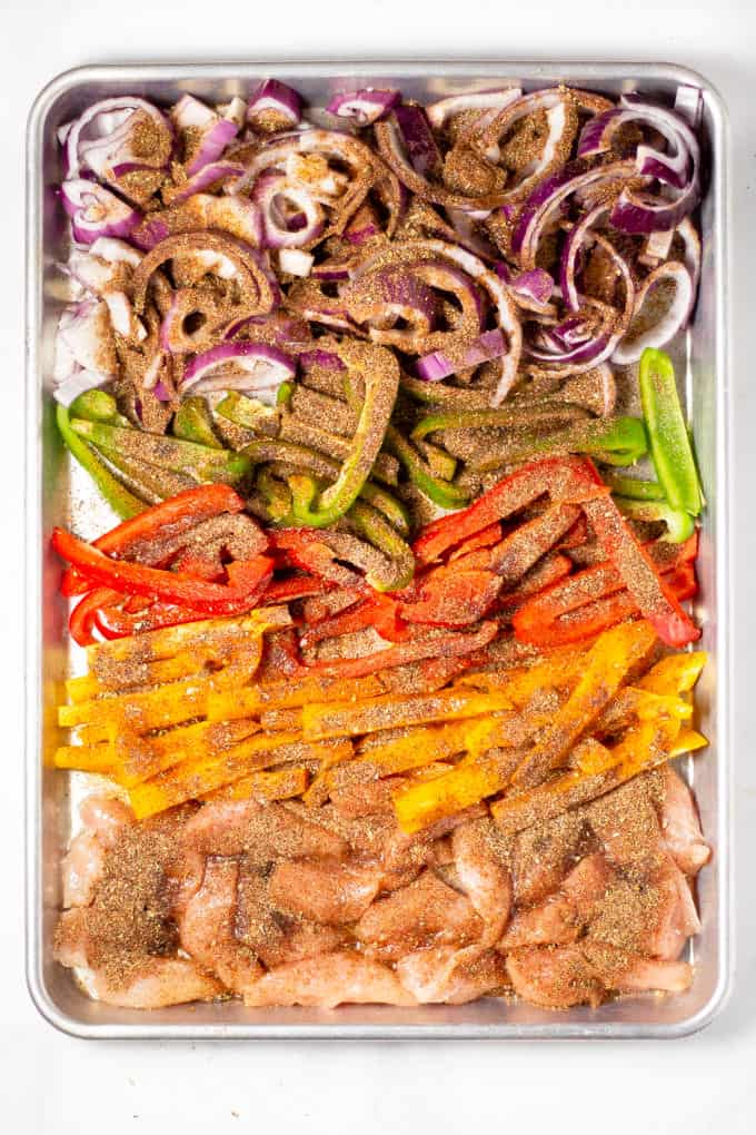 Sheet pan filled with chicken peppers and onions sprinkled with seasoning for sheet pan fajitas