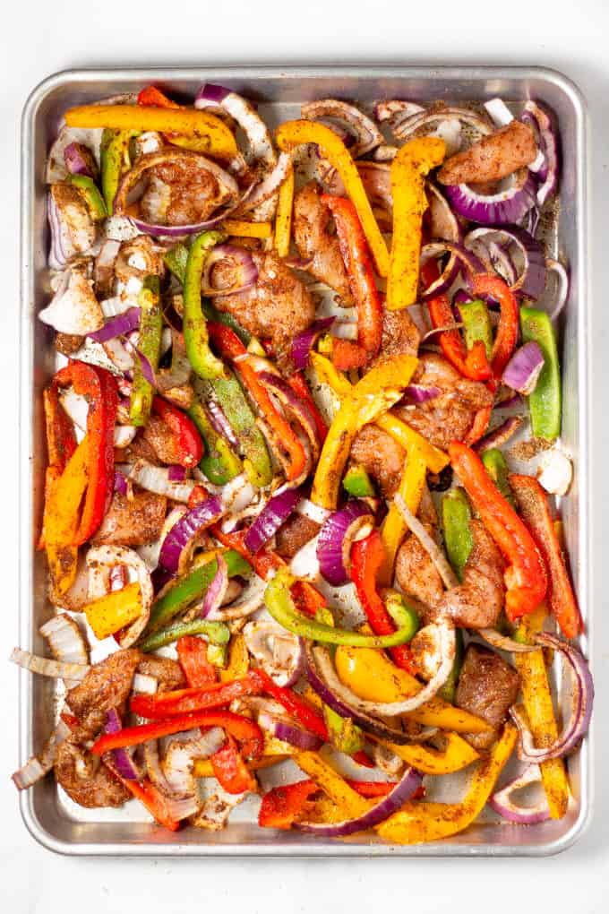 Sheet pan filled with chicken peppers and onions tossed with oil and seasonings for sheet pan fajitas