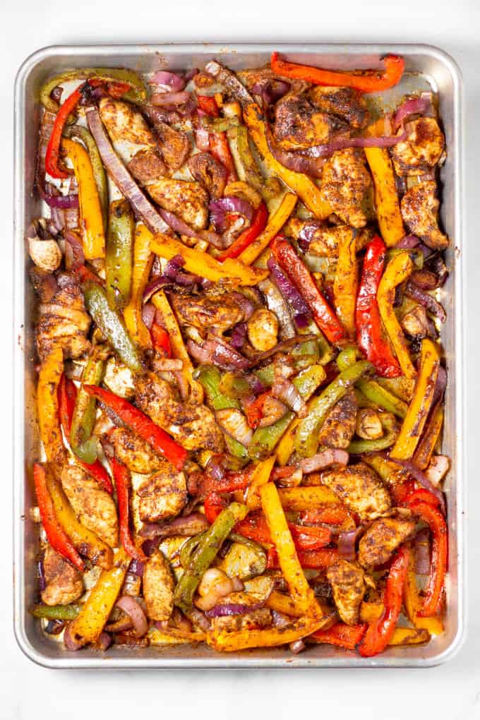 Sheet pan filled with baked chicken peppers and onions for sheet pan fajitas