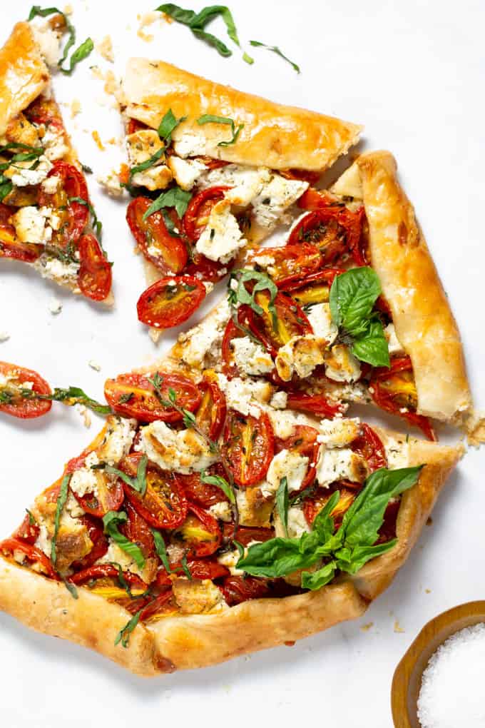 Overhead shot of a freshly baked tomato tart on a white marble counter top garnished with fresh basil