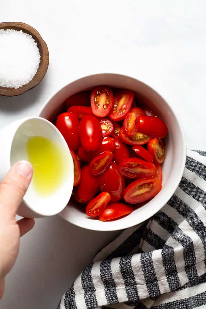 White bowl of tomatoes being drizzled with olive oil