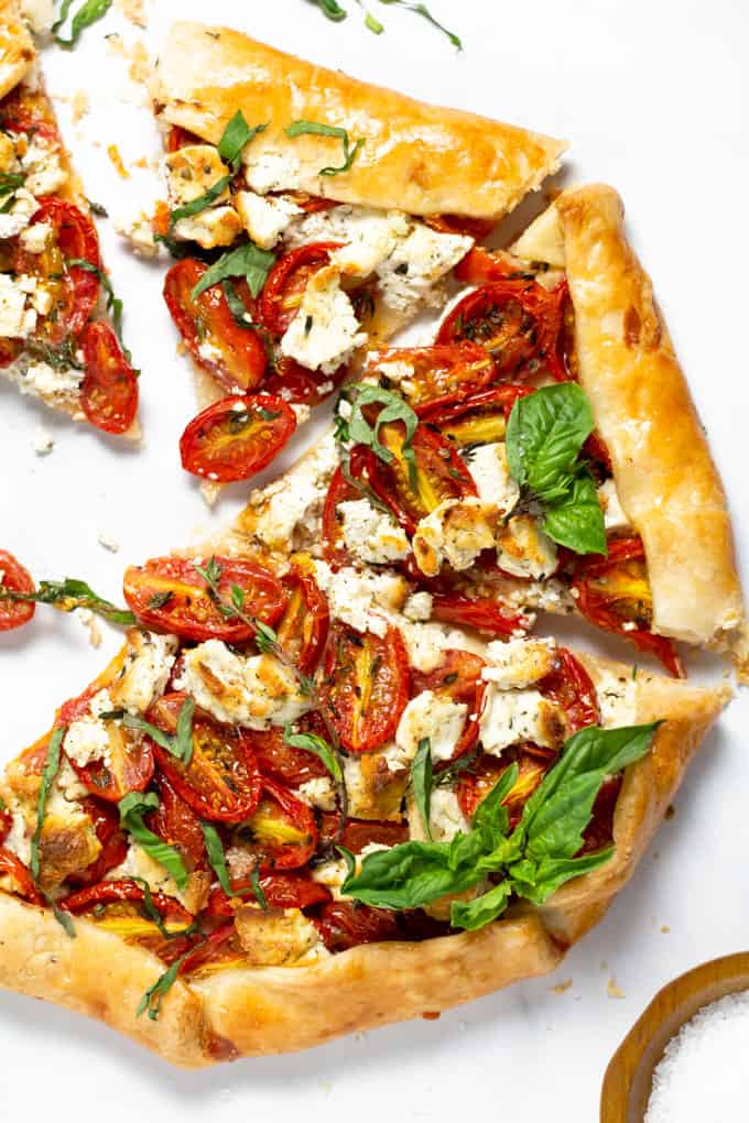 Overhead shot of a tomato tart on a white marble counter top garnished with fresh basil