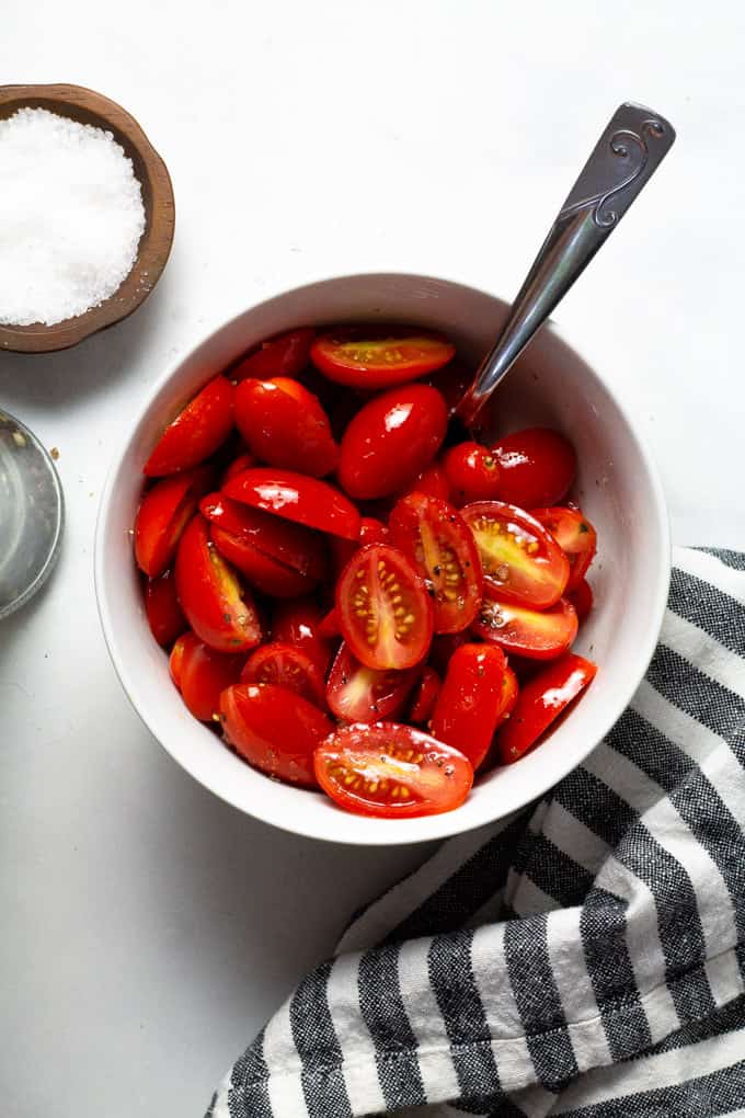 White bowl filled with tomatoes tossed in olive oil salt and pepper