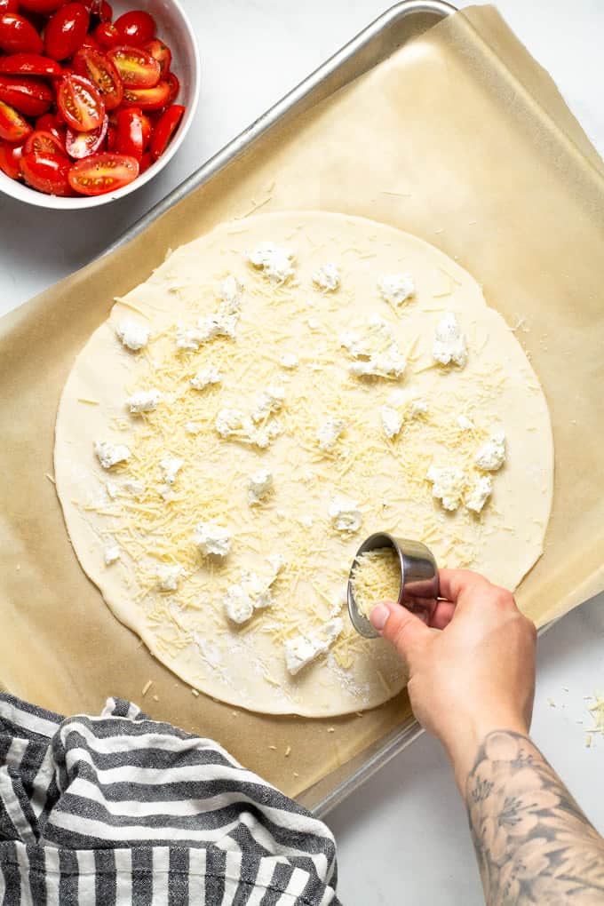 Pie crust on a parchment lined baking sheet being sprinkled with shredded Parmesan