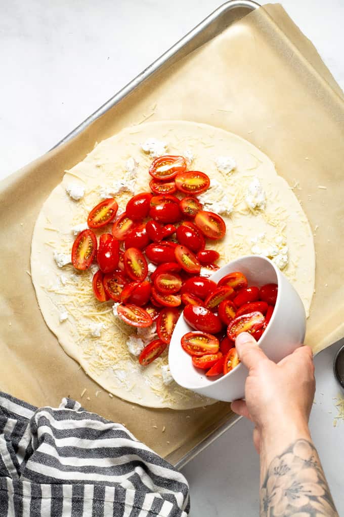 Pie crust on a parchment lined baking sheet with tomatoes being poured onto it