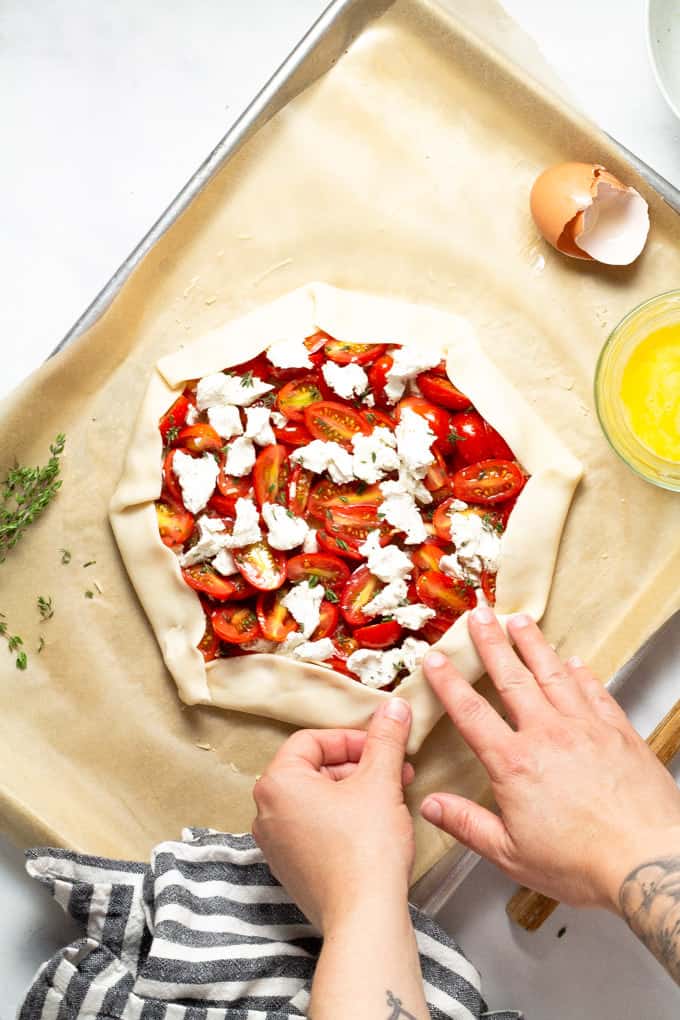 Pie crust topped with goat cheese Parmesan cheese and grape tomatoes with the edges of the crust being folded towards the center