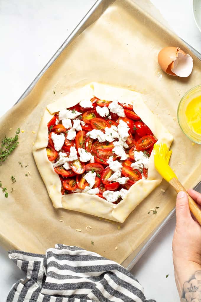 Tomato tart on a parchment lined baking sheet with the crust being brushed with egg wash