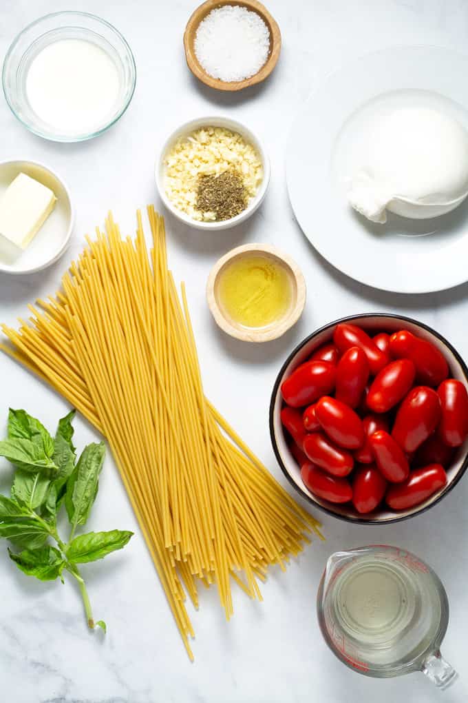 A white marble counter top filled with ingredients to make tomato and garlic pasta