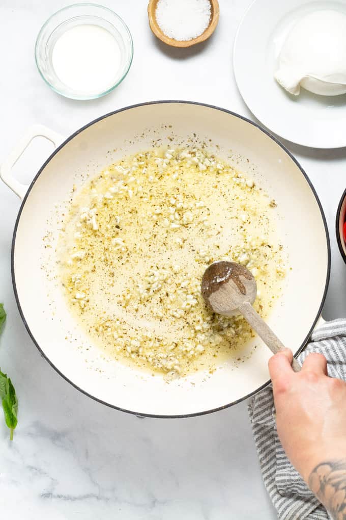 A wooden spoon stirring a pan filled with butter garlic and oregano
