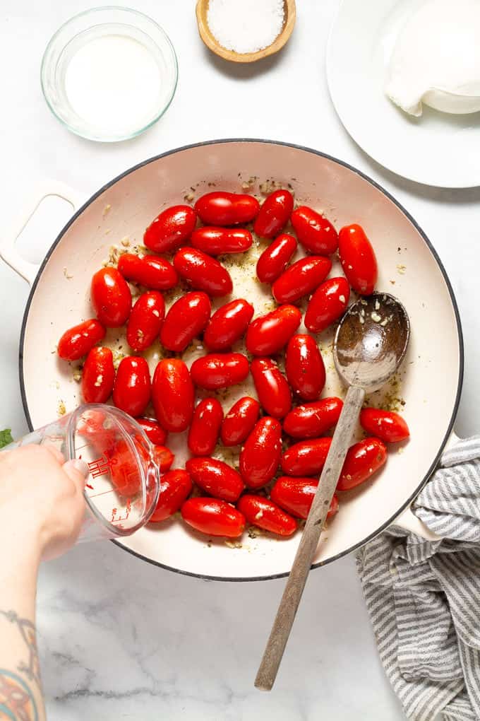 Overhead shot of a pan filled with burst cherry tomatoes and white wine being poured into the pan