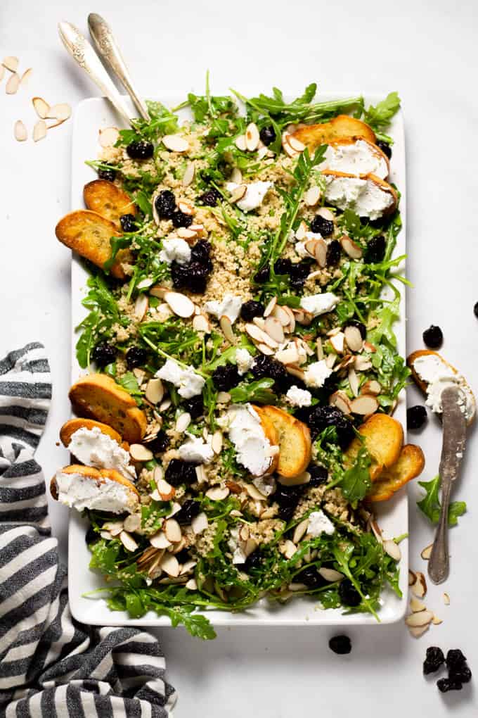 White serving platter filled with arugula salad with goat cheese dried cherries and almonds