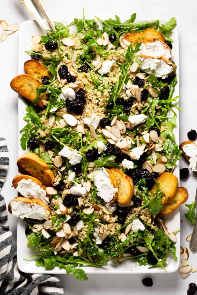 White serving platter filled with arugula salad with goat cheese dried cherries and almonds
