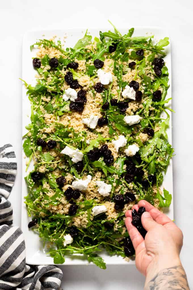 White serving platter filled with arugula salad with couscous goat cheese and cherries