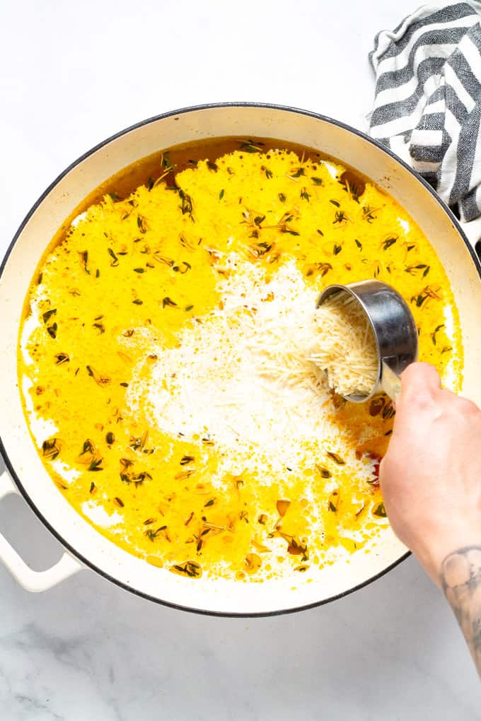 A large saute pan filled with veggies broth and cream with Parmesan cheese being added in