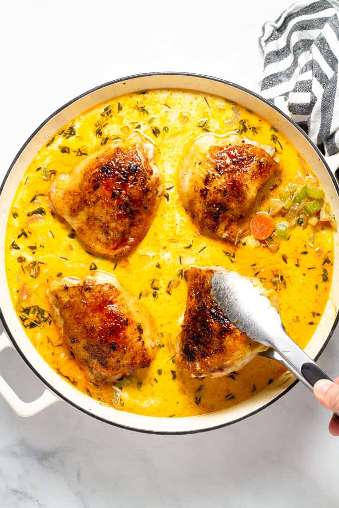 A large saute pan with rice veggies and broth with tongs adding seared chicken thighs to the pan