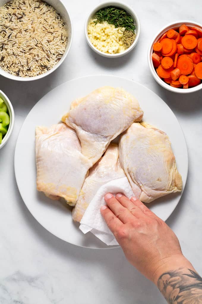 Chicken thighs on a white plate with a hand using a paper towel to dry the chicken skins