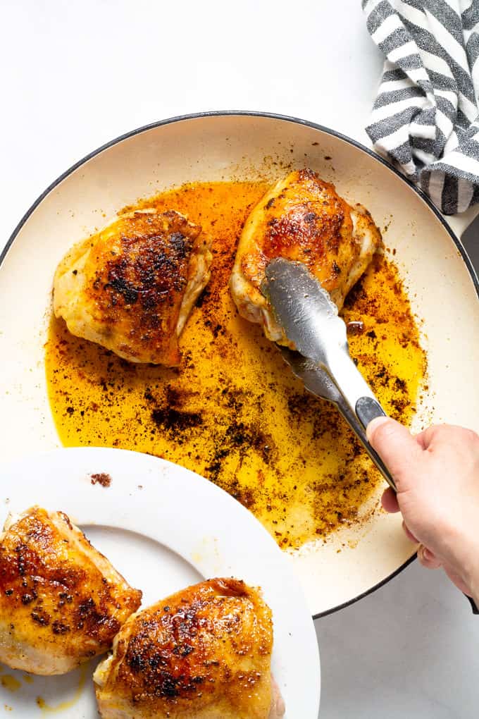 Tongs removing seared chicken thighs from a large pan