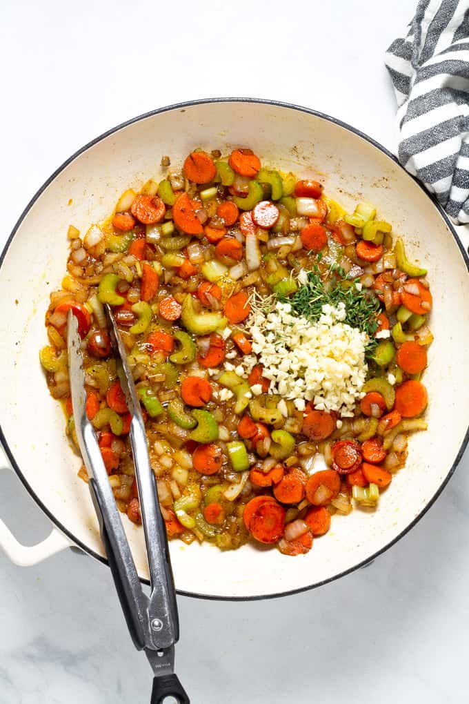 A large saute pan filled with cooked carrots celery and onion and raw garlic and thyme