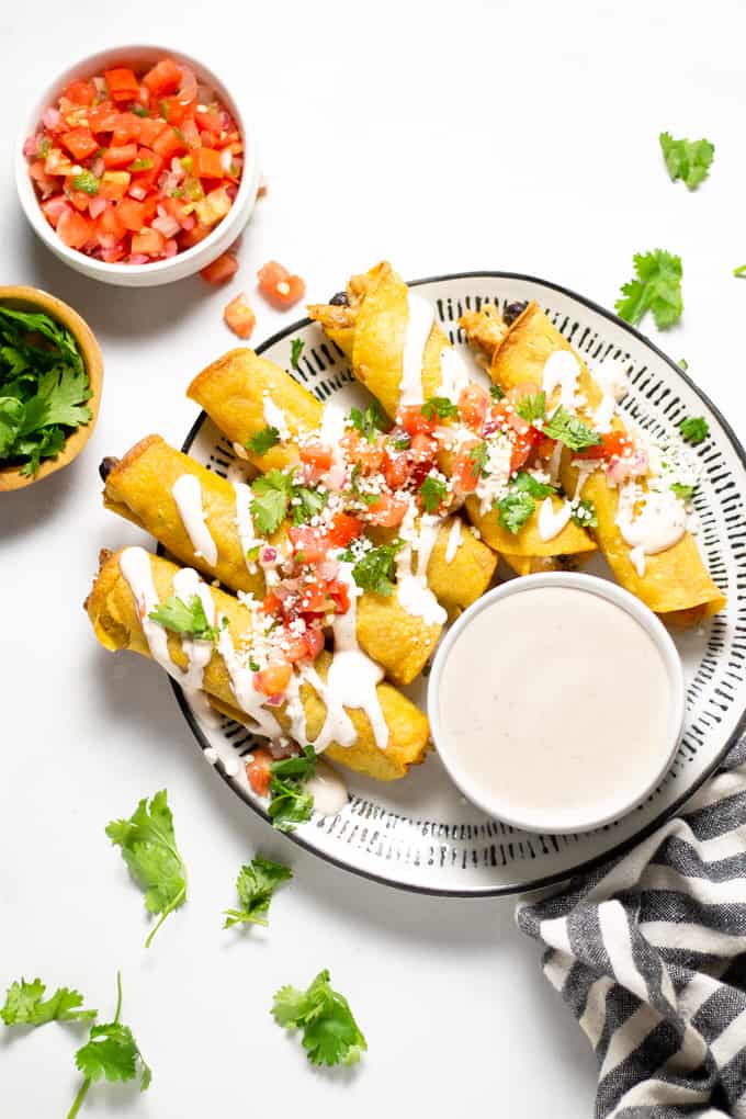 Overhead shot of chicken and black bean taquitos garnished with fresh pico de gallo and queso fresco along with chopped cilantro