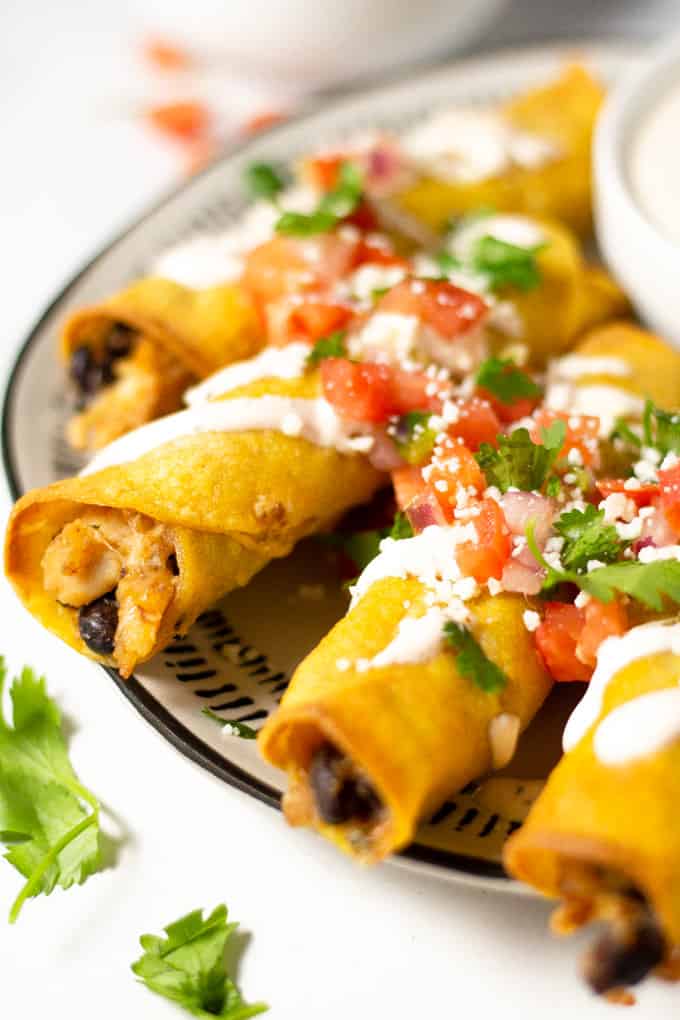 Close up shot of chicken and black bean taquitos garnished with fresh pico de gallo and queso fresco along with chopped cilantro