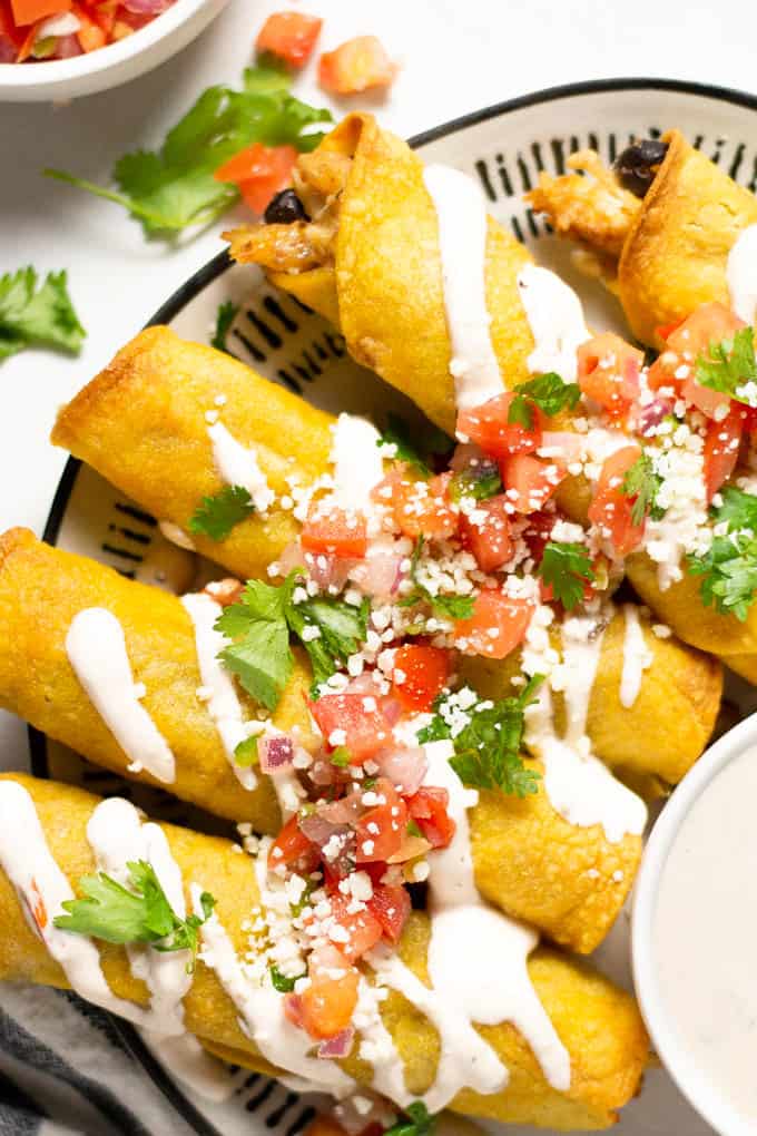 Overhead shot of chicken and black bean taquitos garnished with fresh pico de gallo and queso fresco along with chopped cilantro