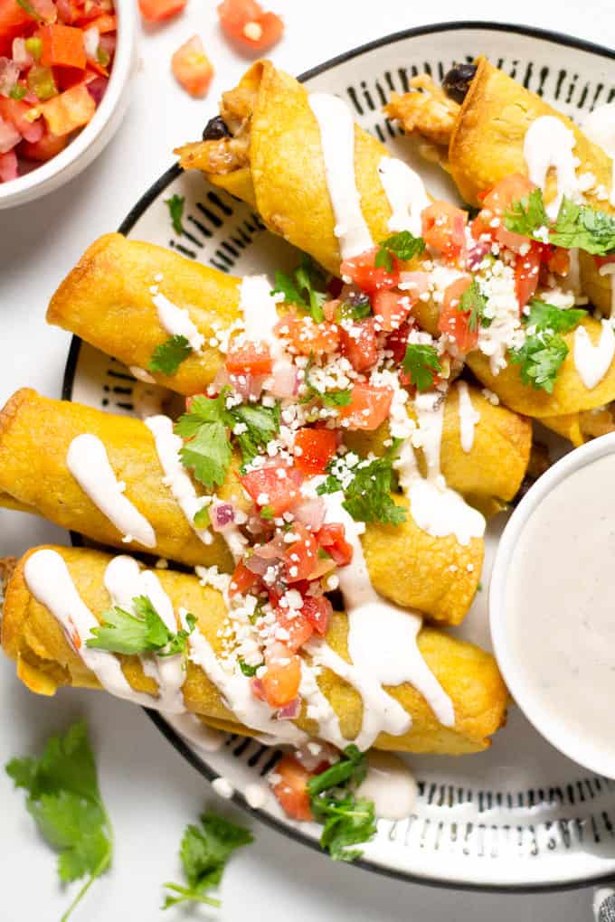 Overhead shot of chicken and black bean taquitos garnished with fresh pico de gallo and queso fresco along with chopped cilantro