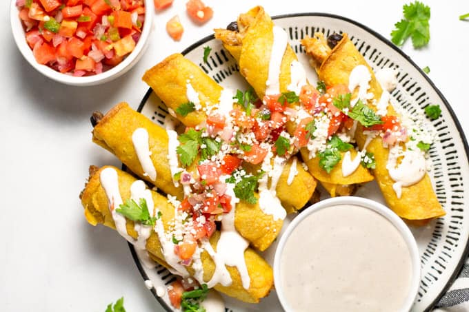 Overhead shot of chicken and black bean taquitos garnished with fresh pico de gallo and queso fresco along with chopped cilantro