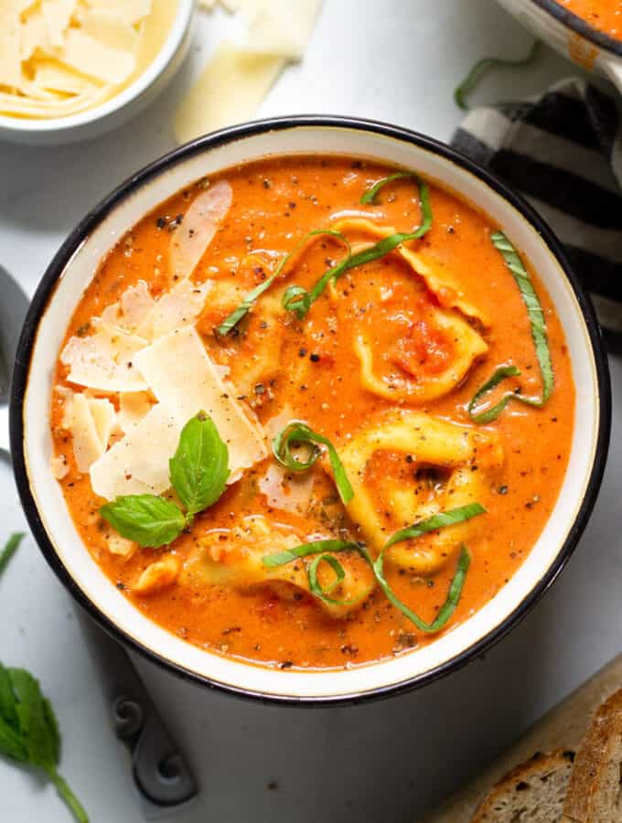 Overhead shot of a bowl of tomato tortellini soup garnished with fresh basil and Parmesan cheese