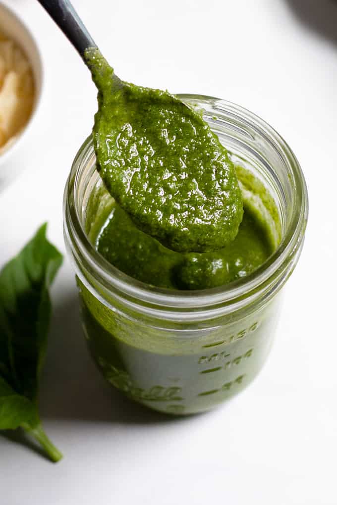 A spoon scooping homemade basil pesto out of a small mason jar