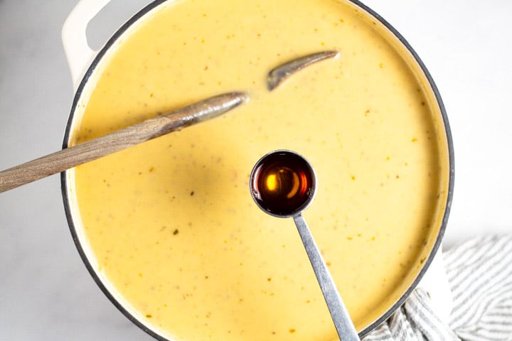 White dutch oven filled with creamy soup an a tablespoon of vinegar being added to it