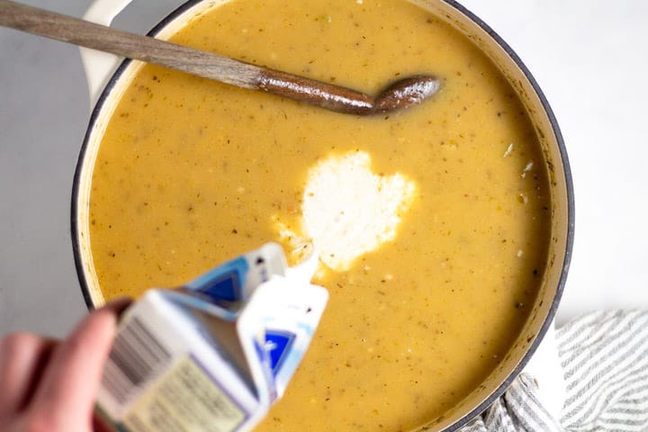 White dutch oven with heavy cream being poured into creamy potato soup