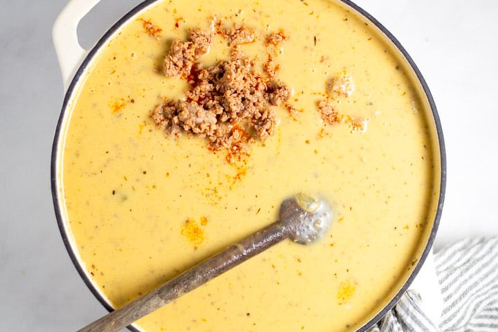 White dutch oven filled with creamy beer cheese potato soup with sausage