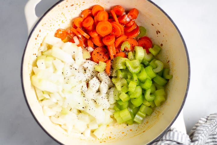 White dutch oven with carrots onion and celery in it