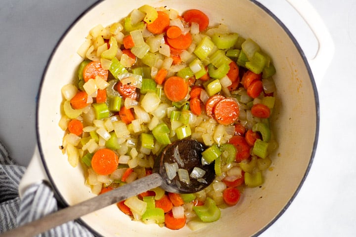 White dutch oven with cooked carrots onion and celery in it