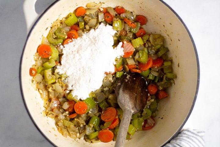 White dutch oven with cooked veggies and flour in it