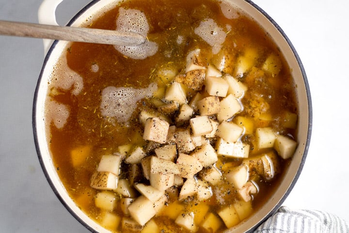 White dutch oven with chicken broth and diced potatoes in it