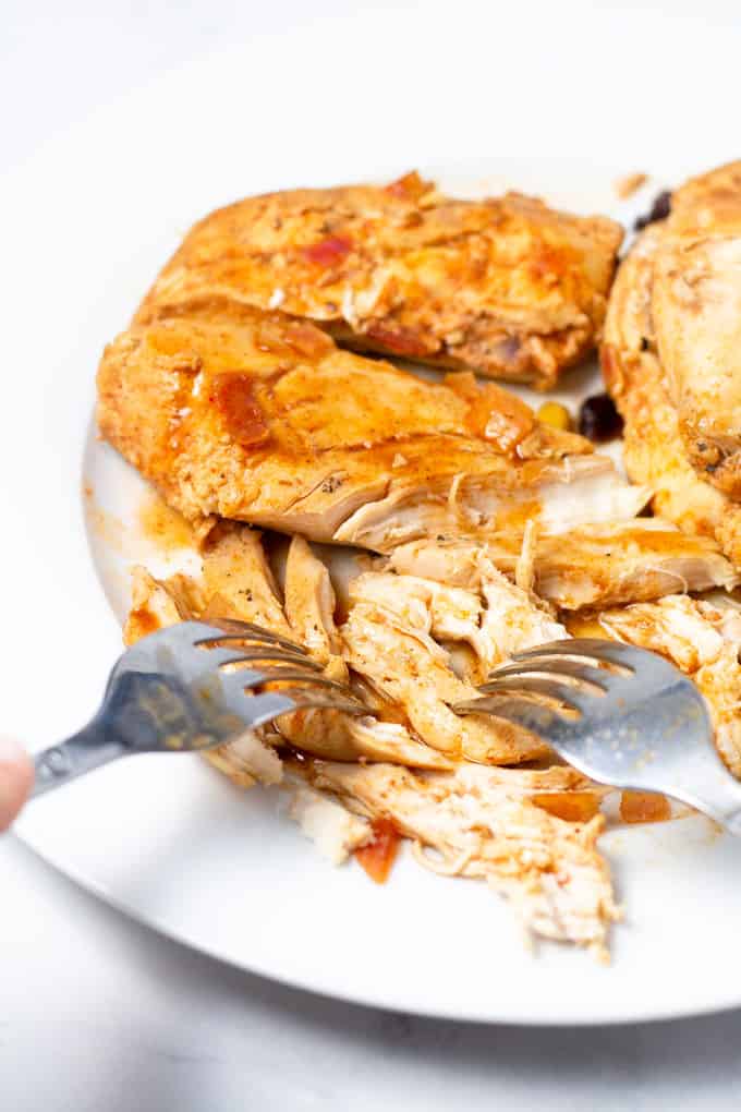White plate filled with shredded chicken and two forks shredding it