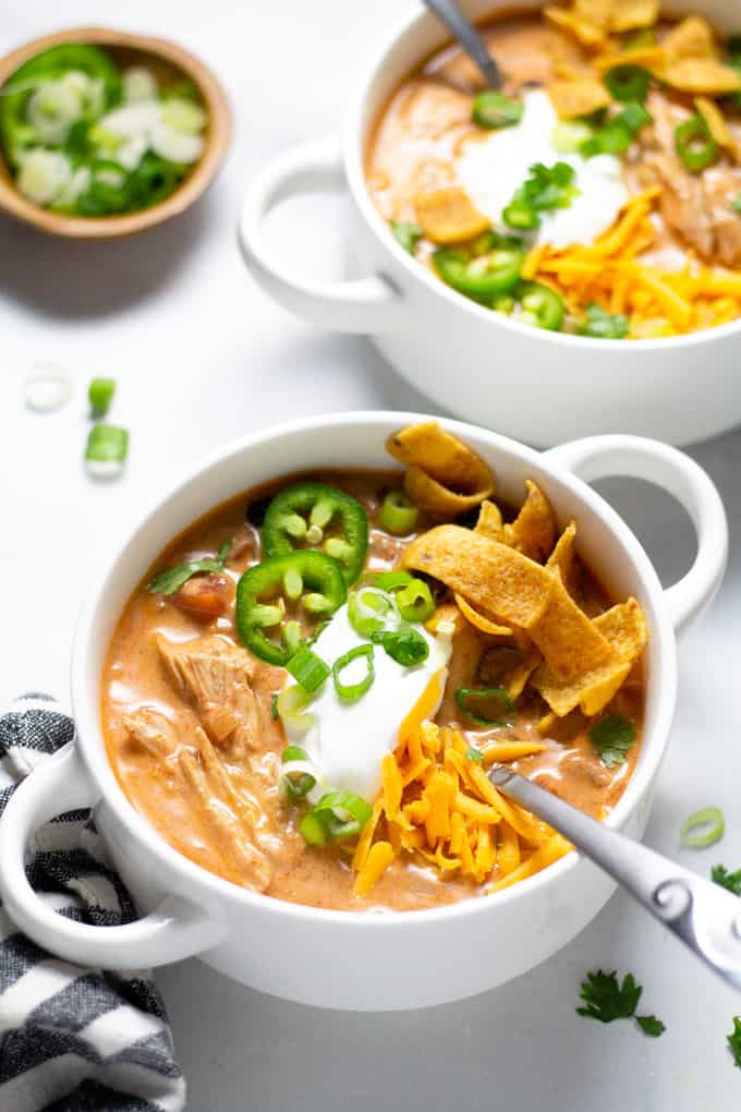 Close up shot of a white bowl filled with slow cooker chicken chili garnished with sour cream and green onions