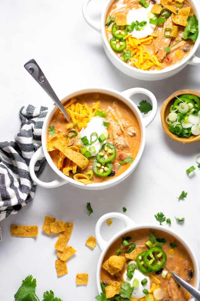 Overhead shot of three white bowls filled with chicken chili garnished with sour cream and green onions
