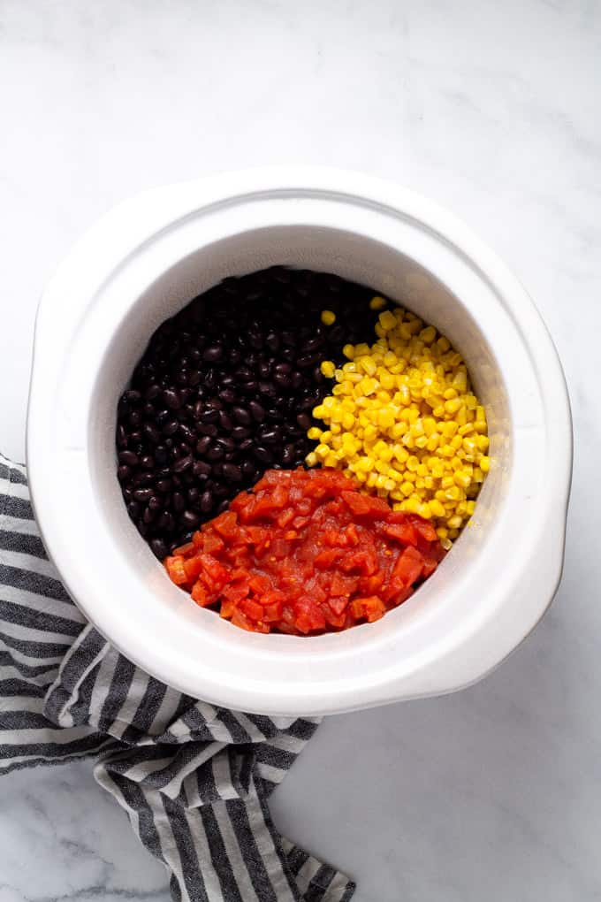 White crock pot insert filled with black beans corn and diced tomatoes