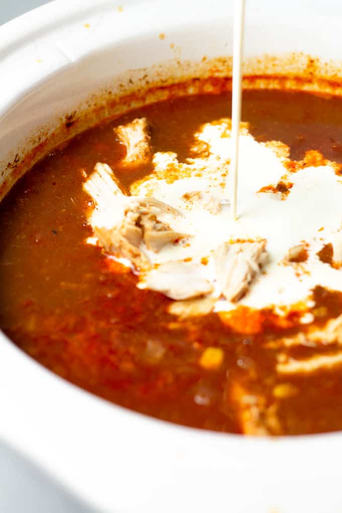 Heavy cream being poured into slow cooker chicken soup