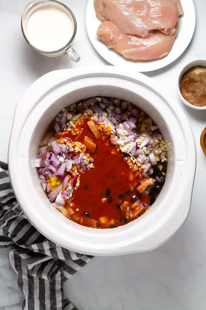 White crock pot insert filled with ingredients to make slow cooker chicken chili