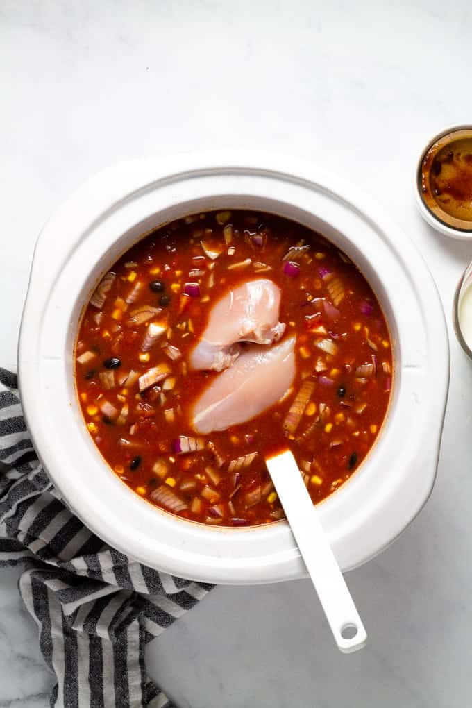 White slow cooker insert with ingredients to make slow cooker chicken chili