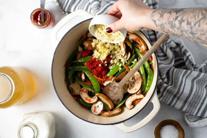 Overhead shot of a white dutch oven with garlic being added to vegetables